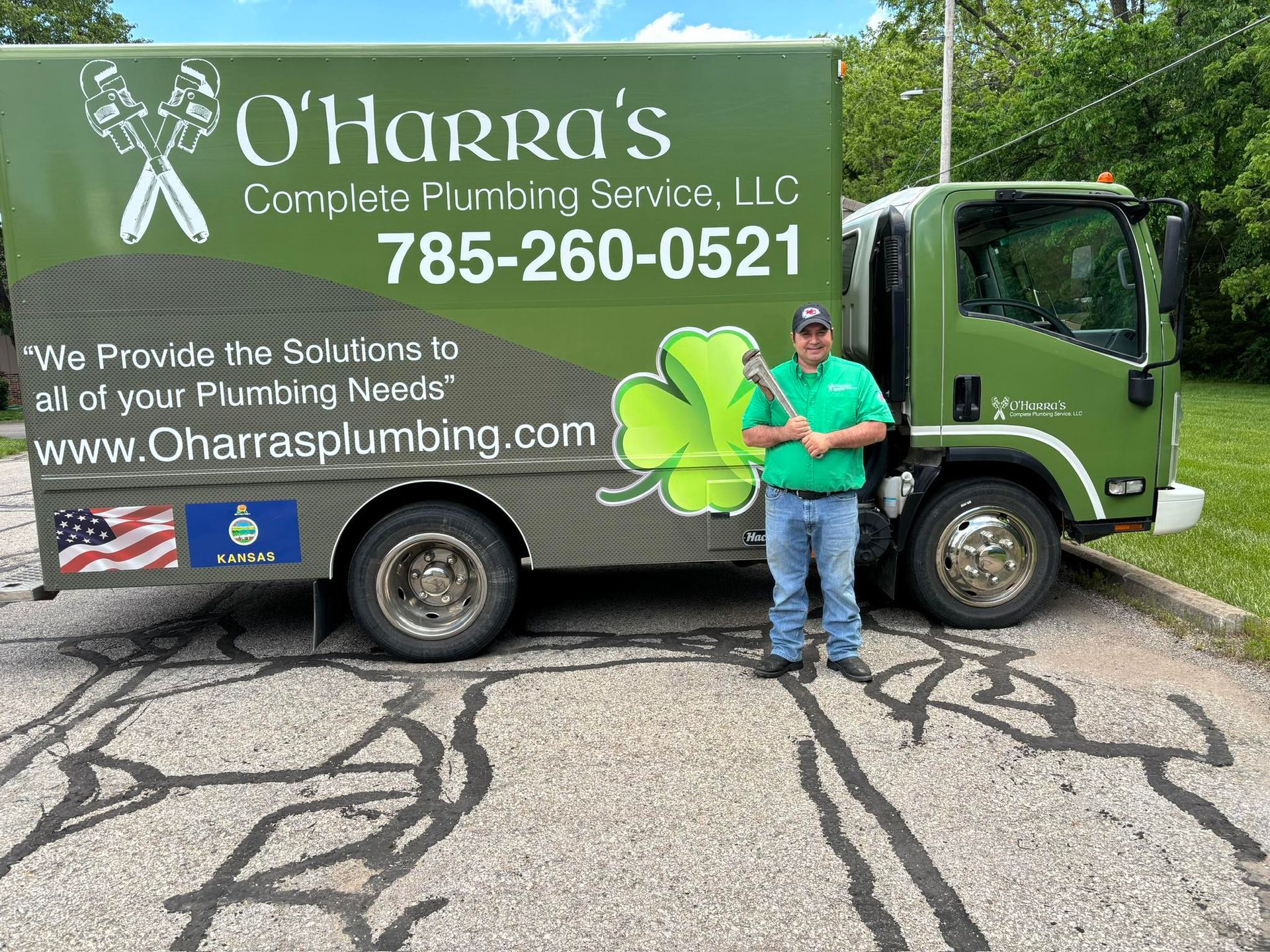 Man standing next to a green O'Harra's plumbing truck with a wrench. The truck has the company's logo and contact info.