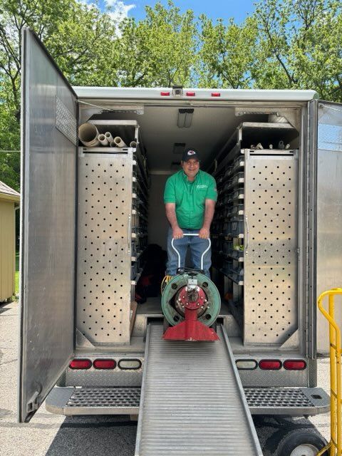 Man inside a trailer, pushing a machine down a ramp. Trailer has shelves and a ramp. Green shirt.