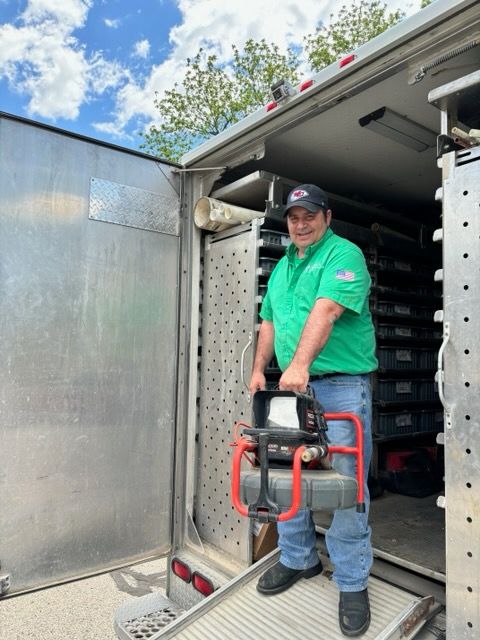 Man in green shirt holds a tool exiting a delivery truck with open doors on a sunny day.
