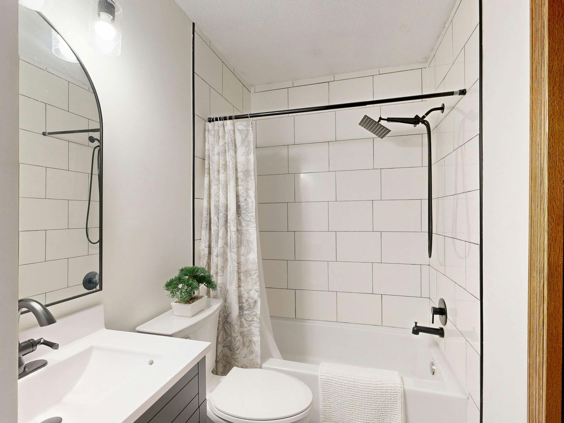 Bathroom with white tile shower, black fixtures, white toilet, and a vanity.