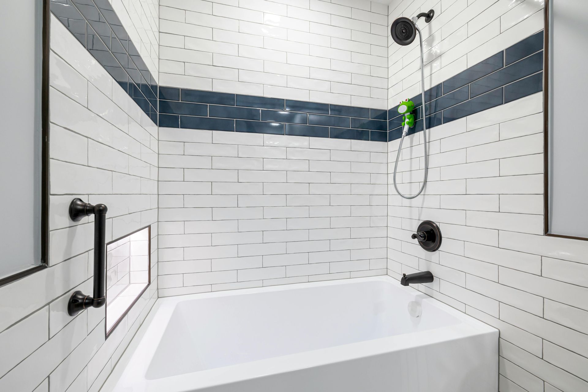 White-tiled bathroom with a blue stripe, a white tub, and black fixtures.