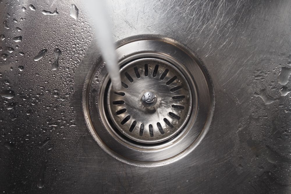 Water flowing into a stainless steel sink drain.