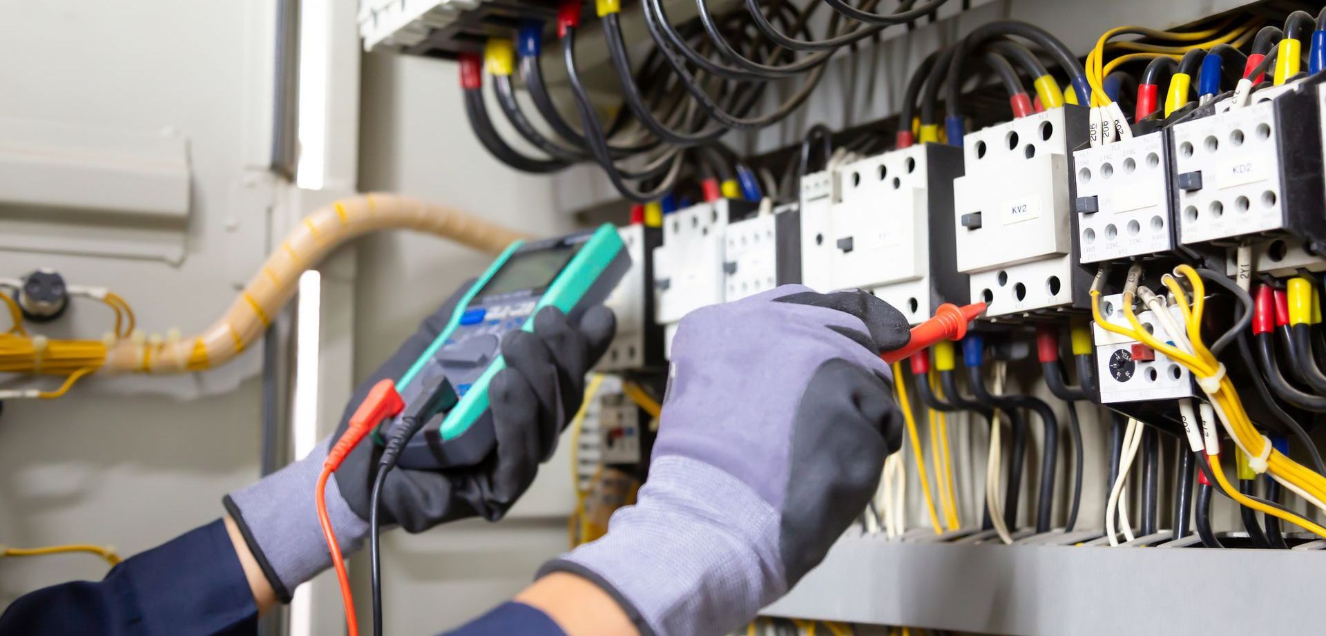An electrician is working on an electrical panel with a multimeter.