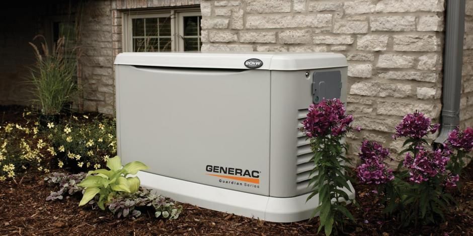 A generator is sitting in front of a brick building next to flowers.