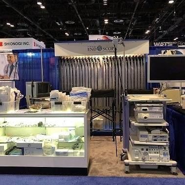 Medical equipment display at a trade show: display cases with supplies, endoscopic equipment cart, and a monitor.