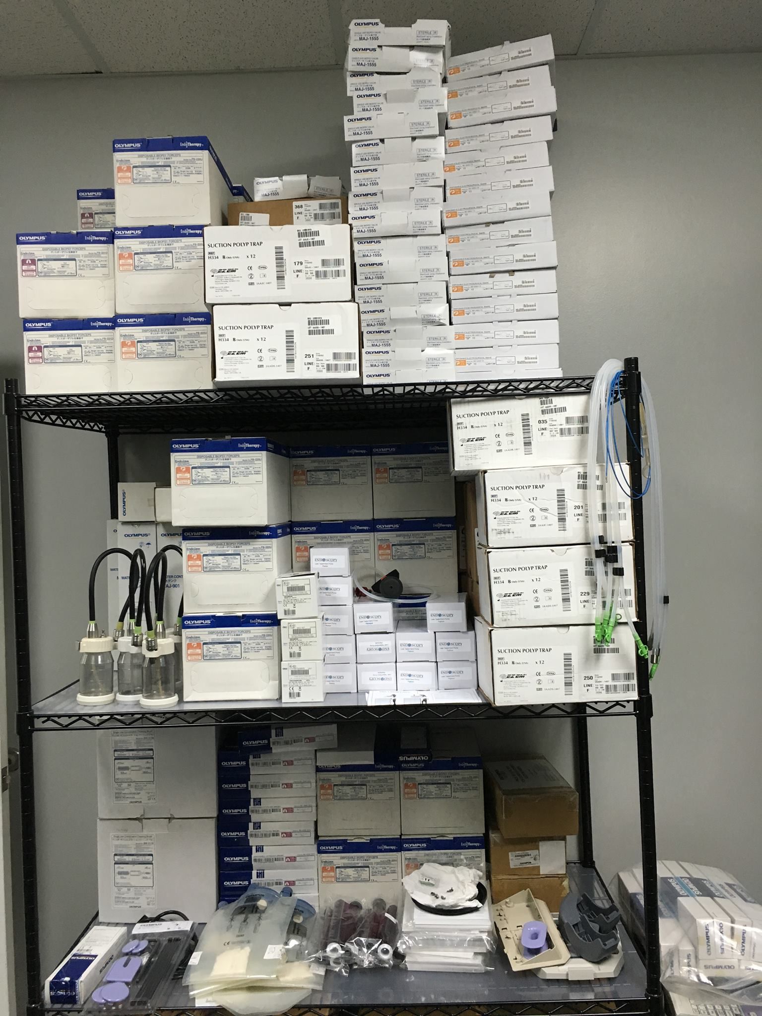 A black metal shelf stacked with various medical supply boxes, tubing, and equipment in a sterile room.