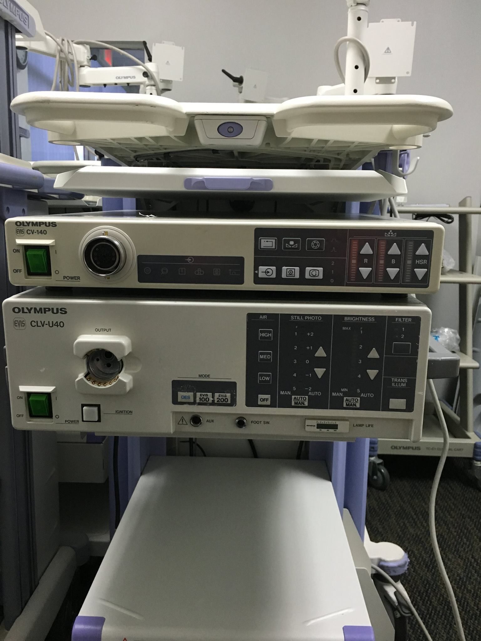 Medical equipment cart with Olympus branded light source and video processor units, in a medical setting.