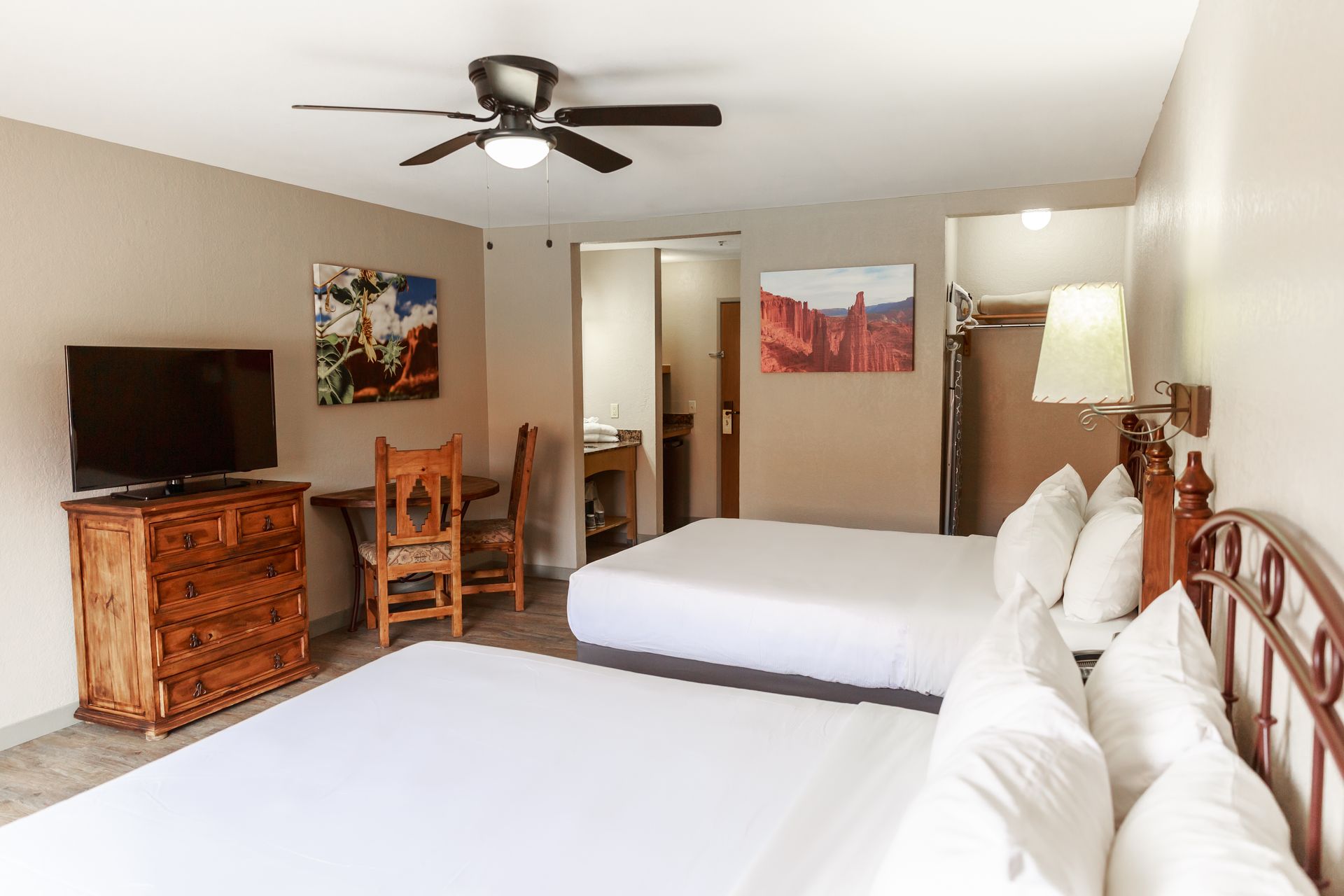 A hotel room with two beds , a dresser , a chair , a television and a ceiling fan.