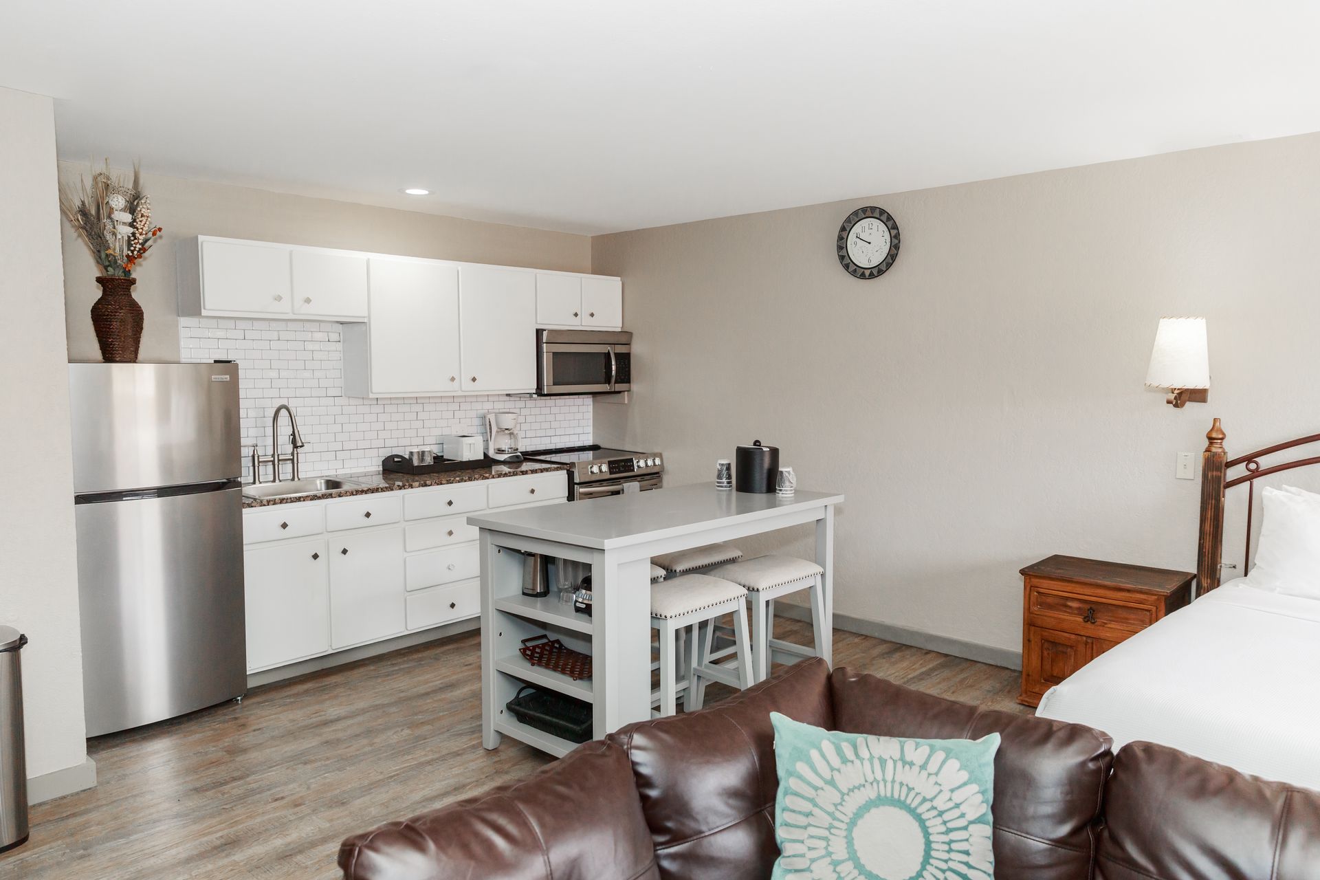 A hotel room with a couch , bed , kitchen and refrigerator.