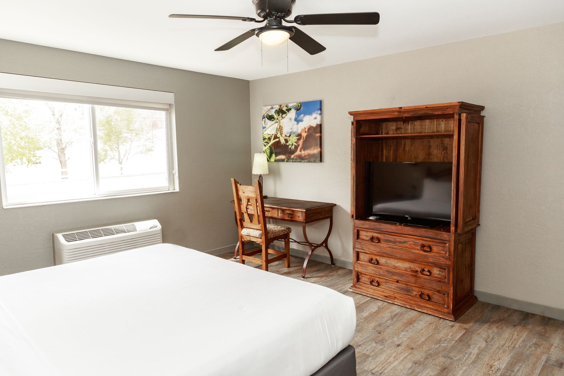 A hotel room with a bed , desk , chair , television and ceiling fan.