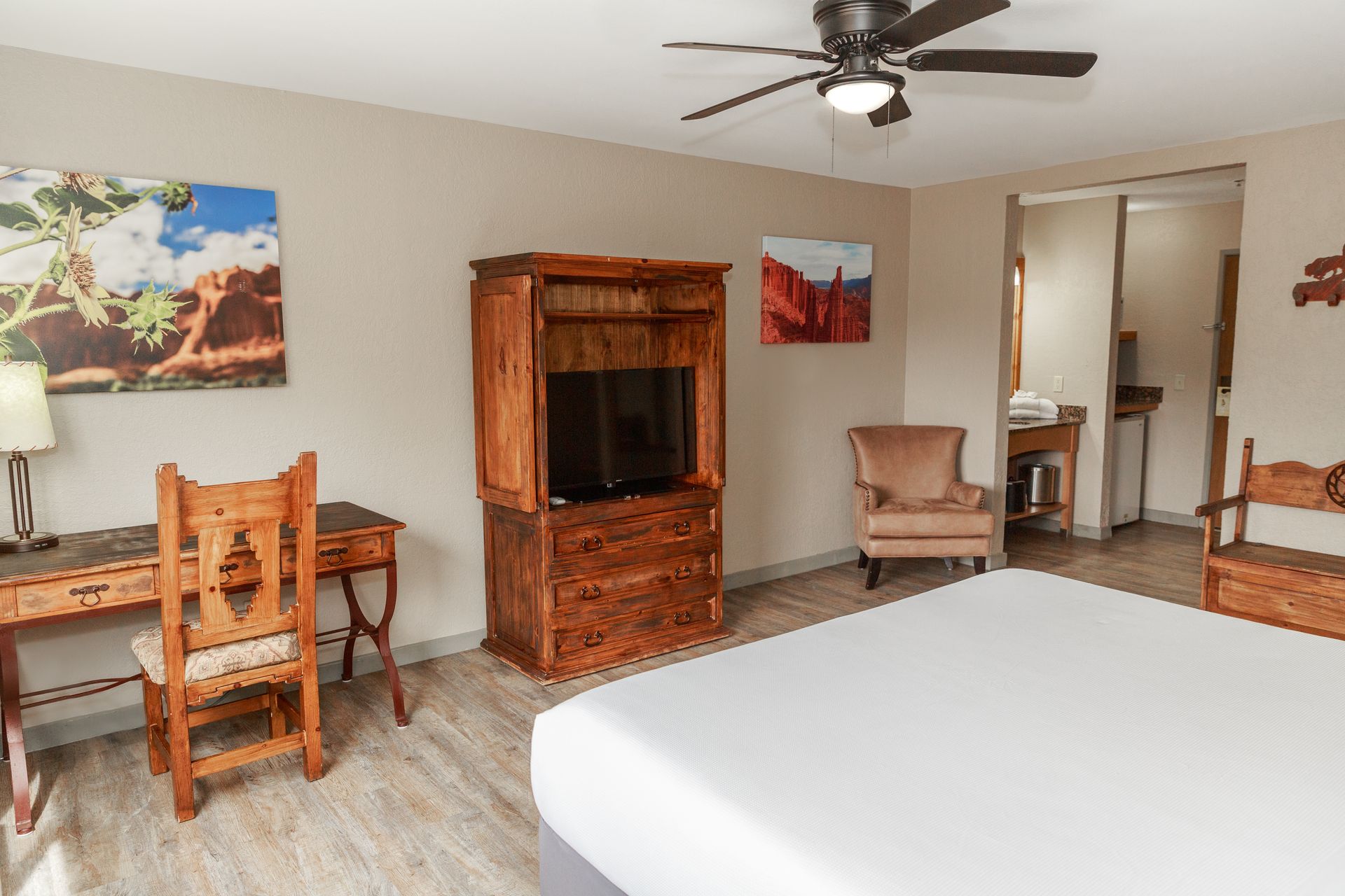 A hotel room with a king size bed , desk , chair , television and ceiling fan.