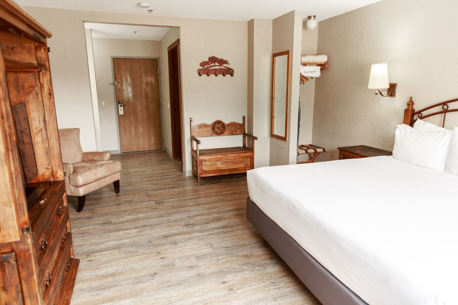 A hotel room with a king size bed , chair , dresser and mirror.