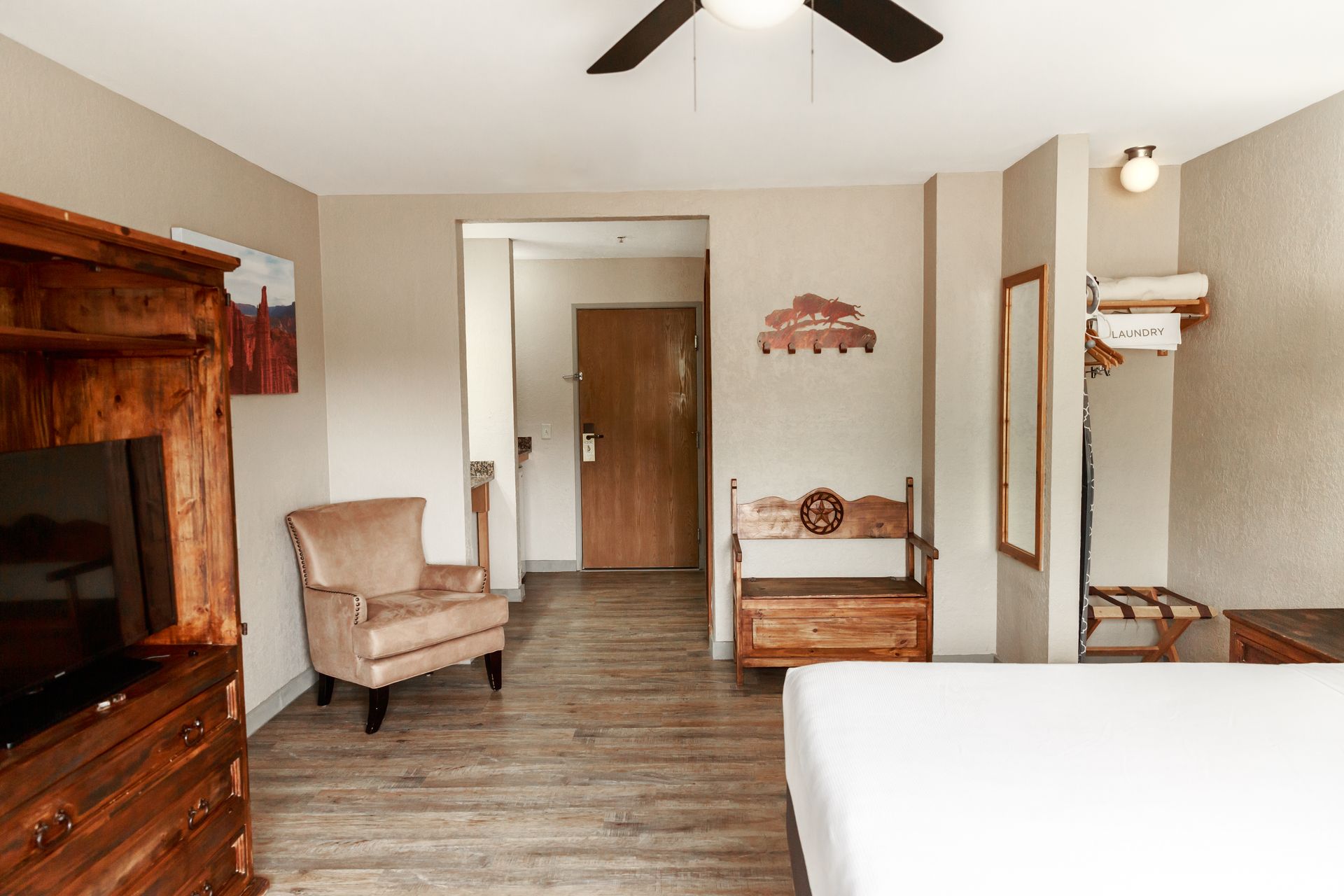A hotel room with a bed , chair , television and ceiling fan.