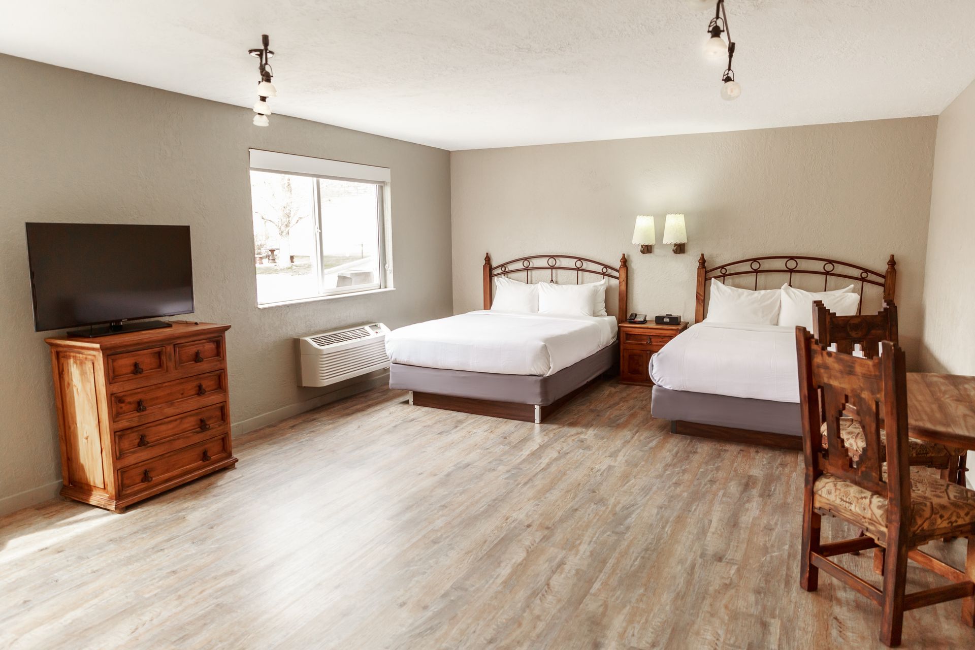 A hotel room with two beds , a dresser and a flat screen tv.