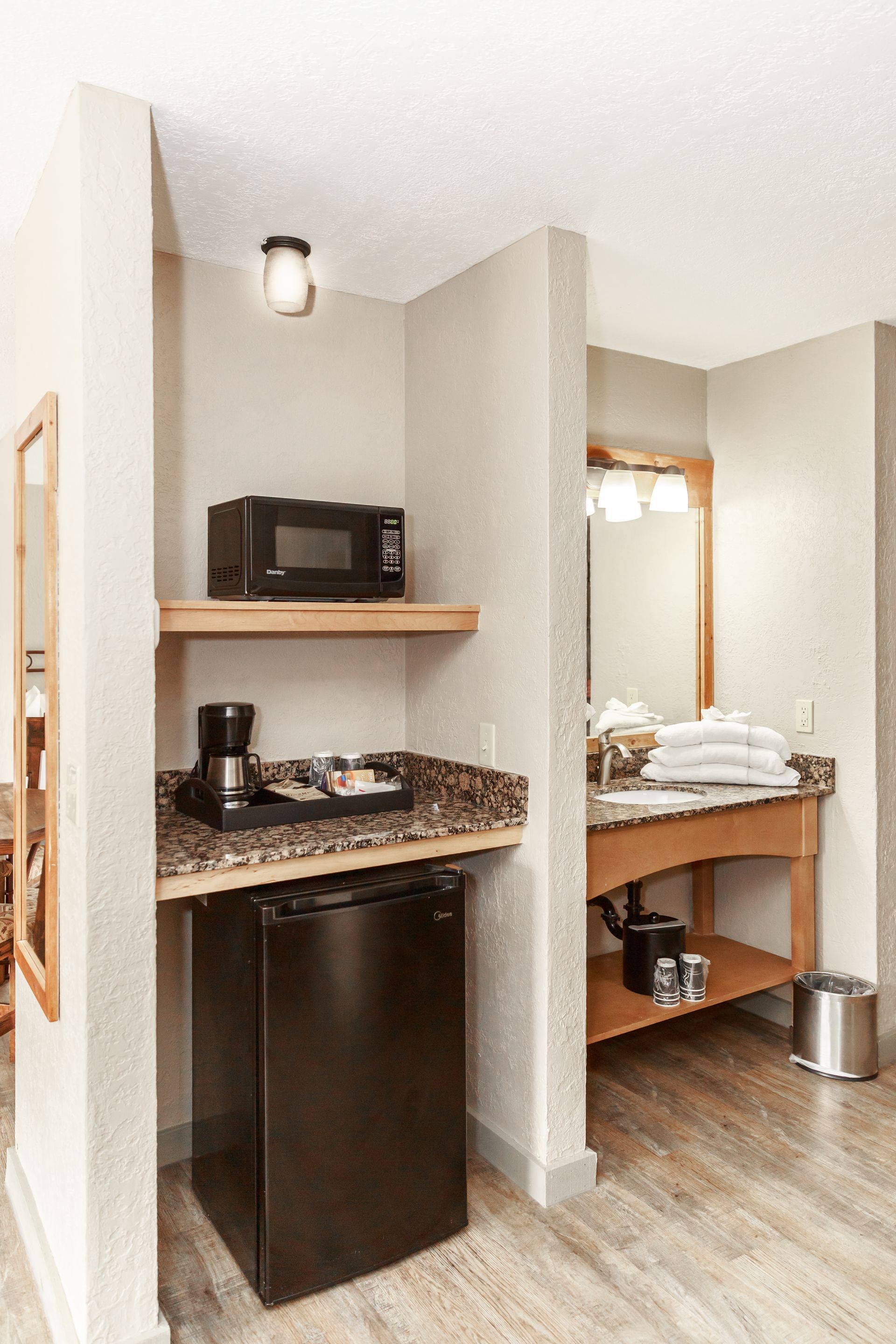 A hotel room with a refrigerator , microwave , coffee maker and sink.