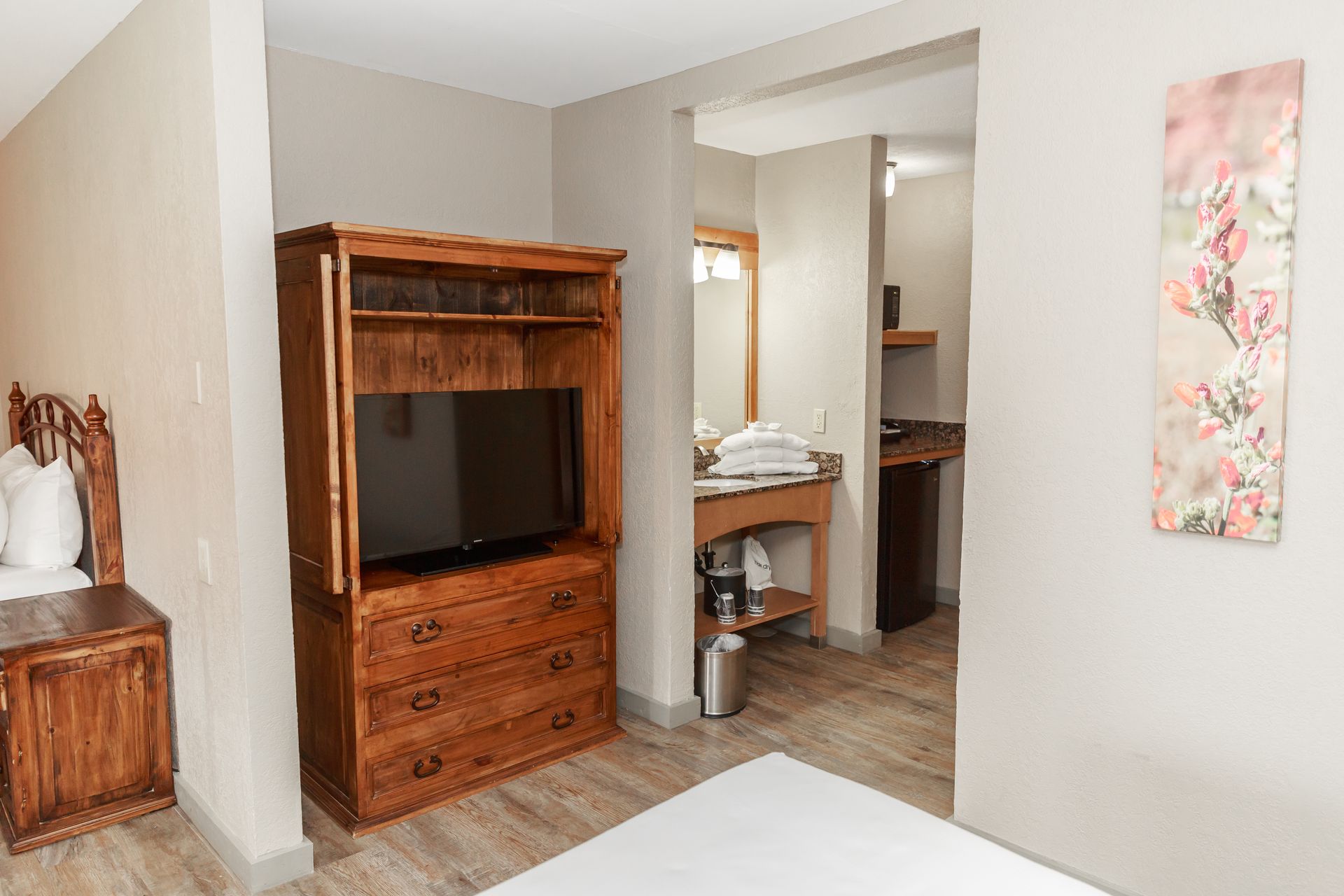 A hotel room with a bed , dresser , television and bathroom.
