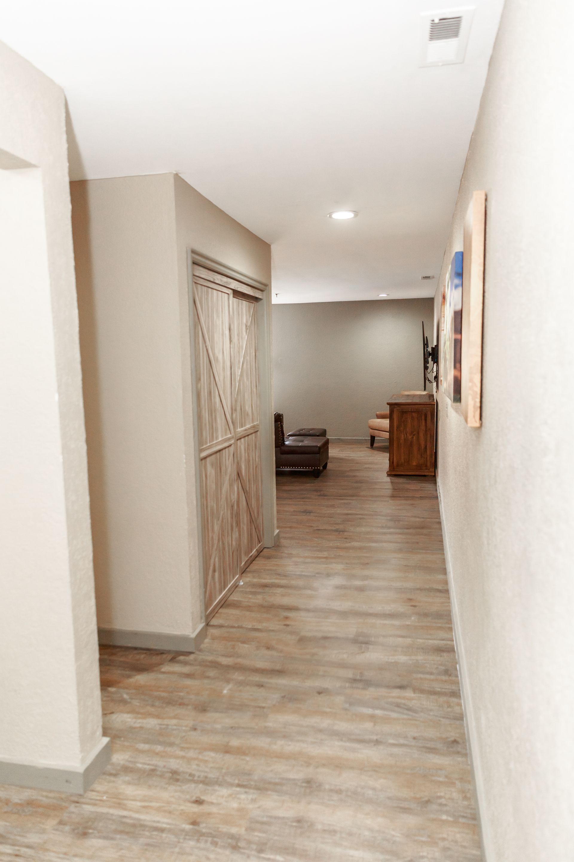 A long hallway with wooden floors and a sliding barn door leading to a living room.