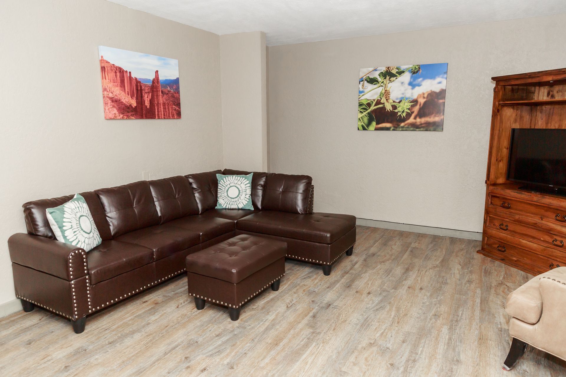 A living room with a large sectional couch , ottoman , chair and television.