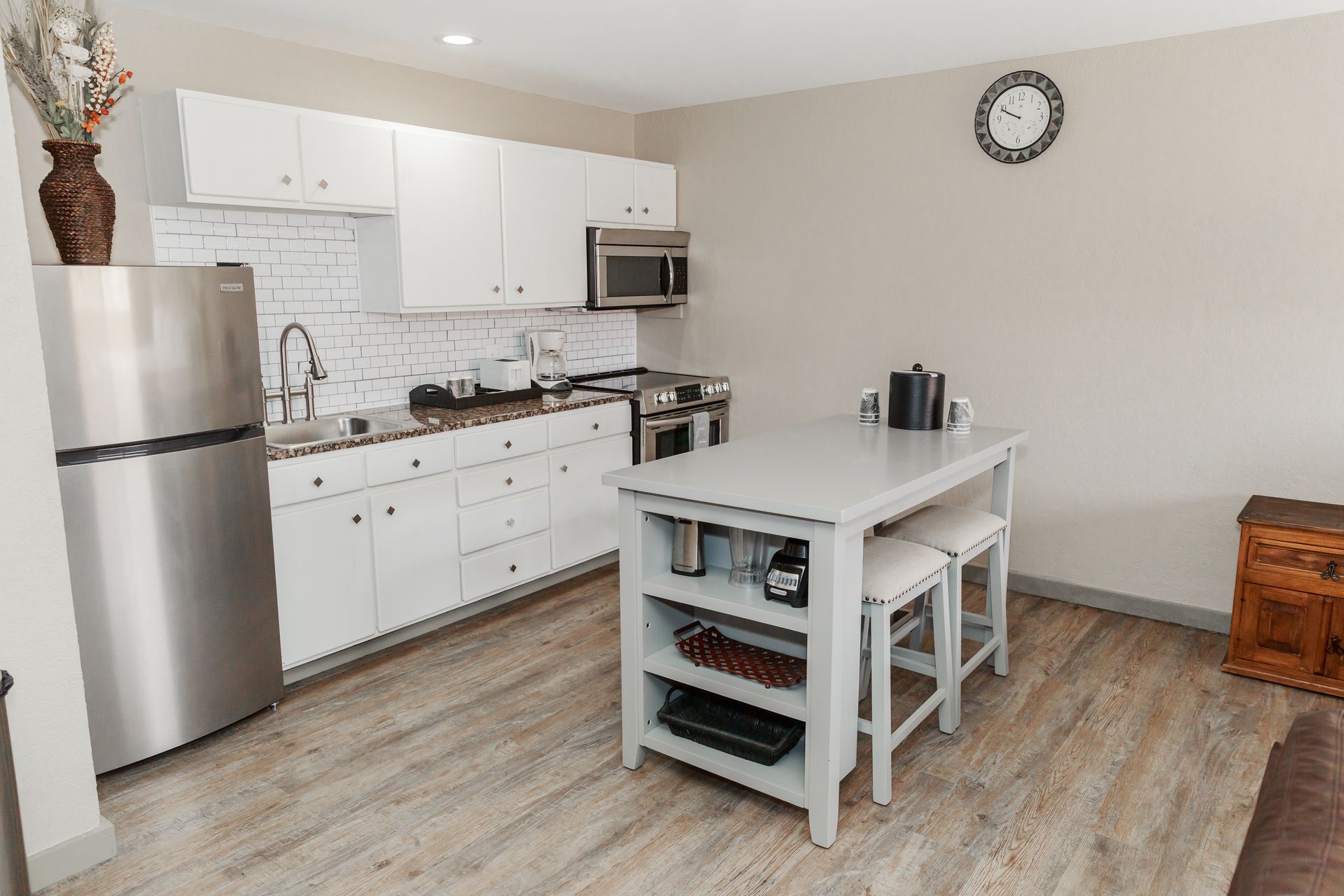 A kitchen with white cabinets , stainless steel appliances , a refrigerator and a table.