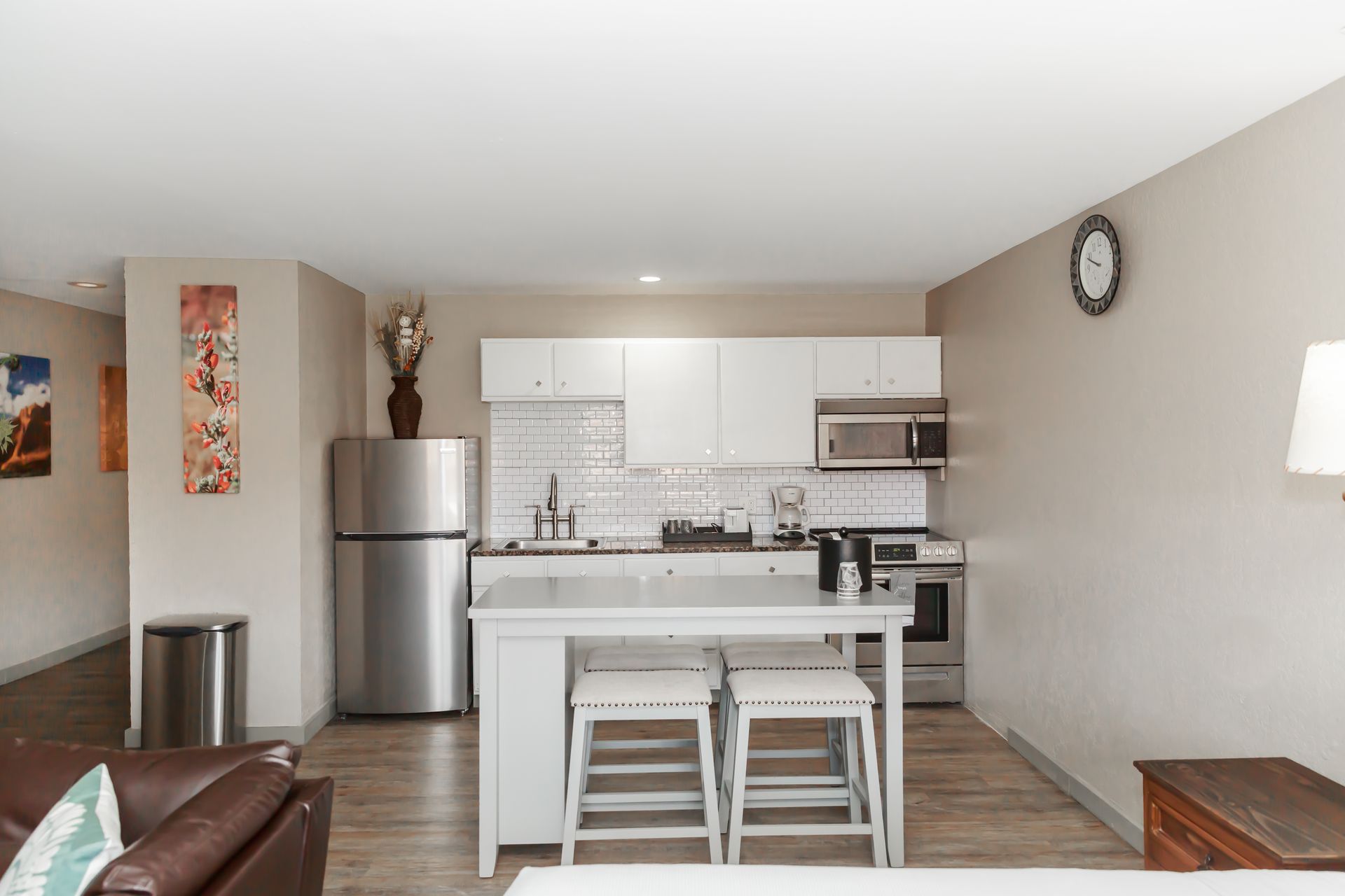 A kitchen with stools , a refrigerator , a microwave , and a clock on the wall.