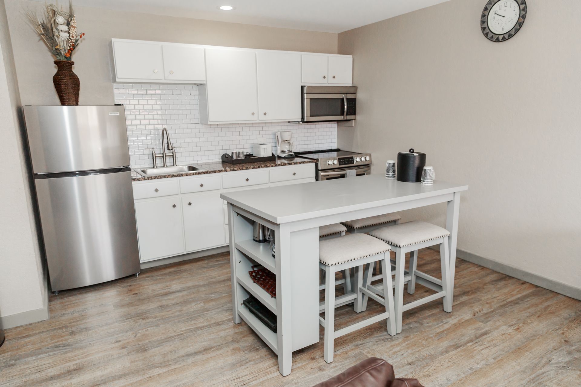 A kitchen with white cabinets , stainless steel appliances , a refrigerator and a table with stools.
