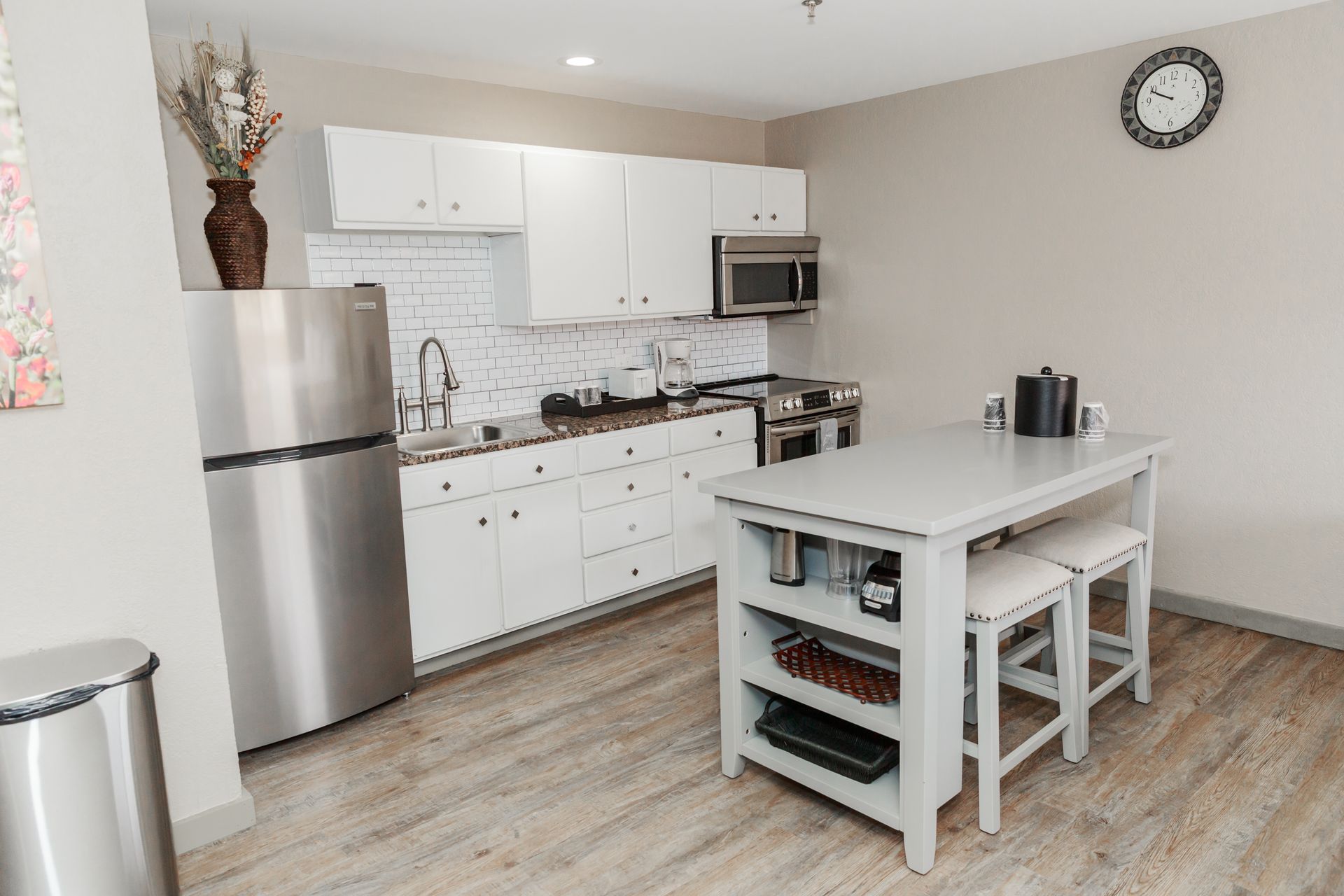 A kitchen with white cabinets , stainless steel appliances , a refrigerator and a table.