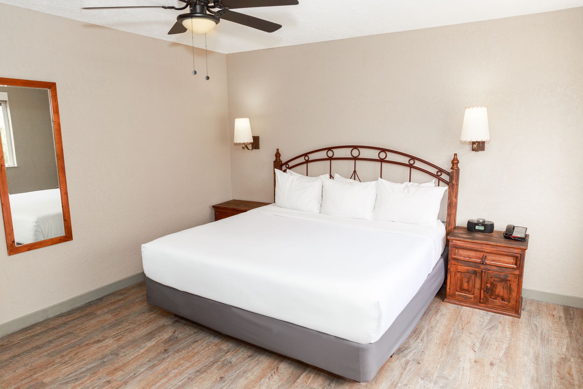 A hotel room with a king size bed , nightstand , mirror and ceiling fan.