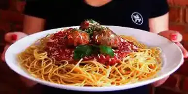 A woman is holding a plate of spaghetti and meatballs.