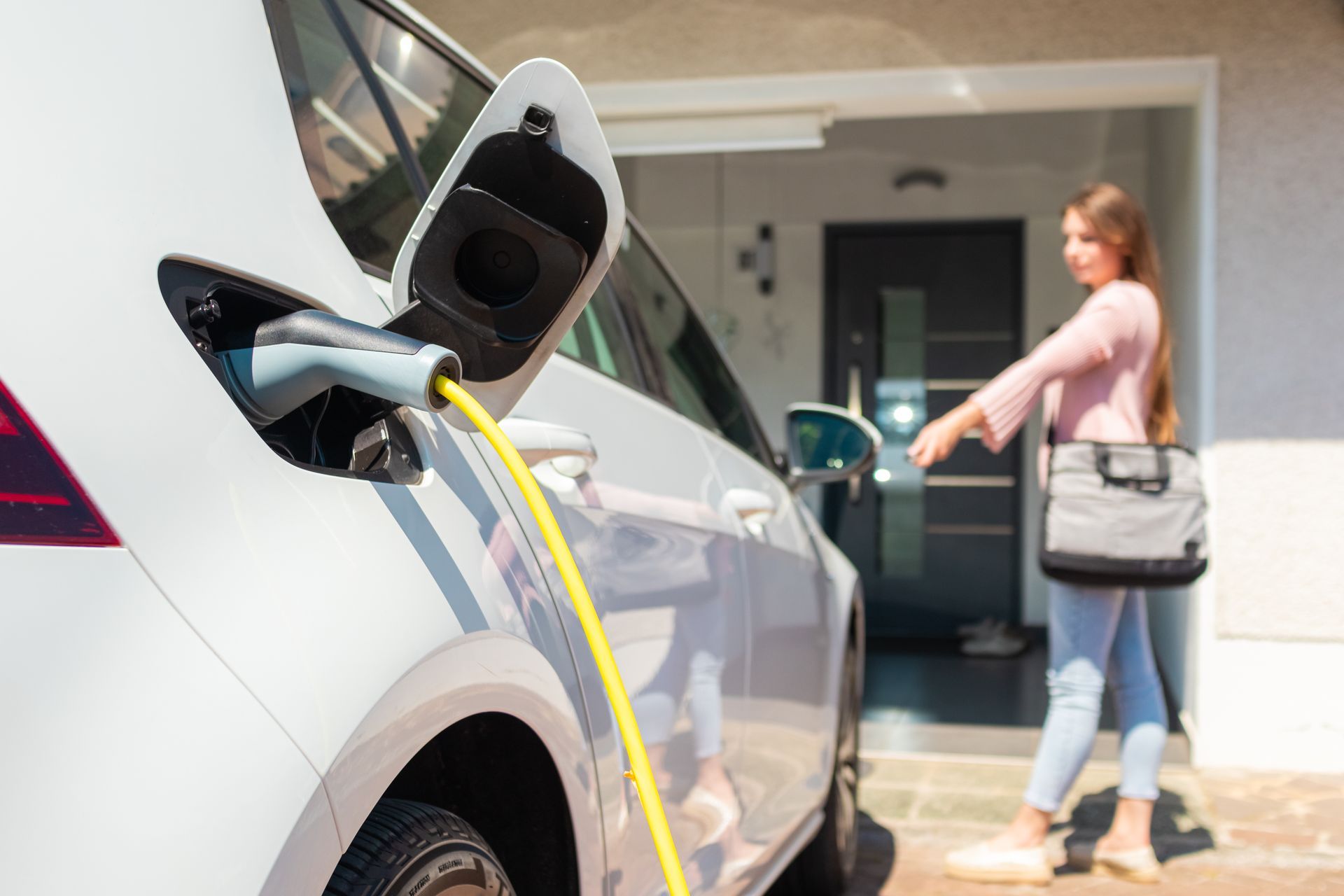 A woman is charging her electric car in front of her house.