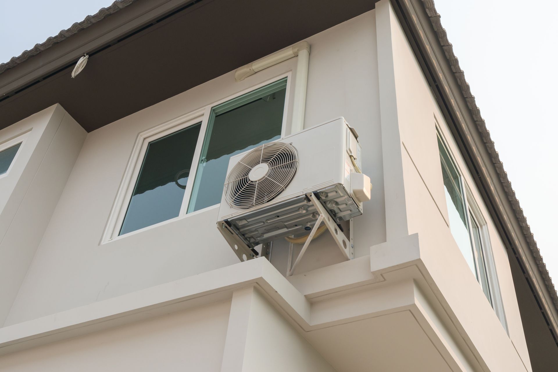 An air conditioner is mounted on the side of a building next to a window.