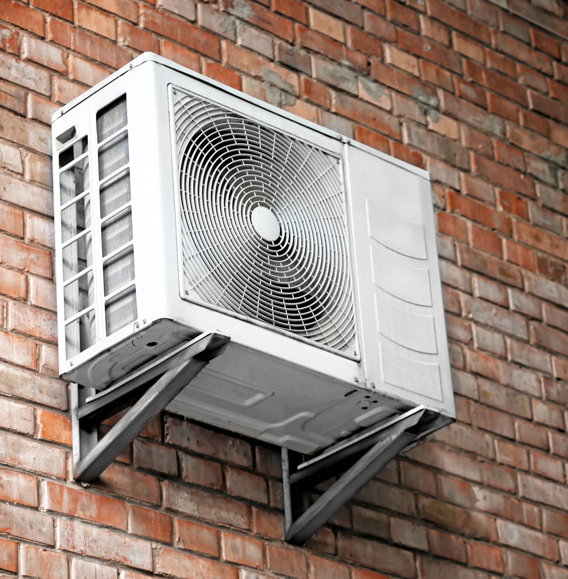 A white air conditioner is mounted on a brick wall