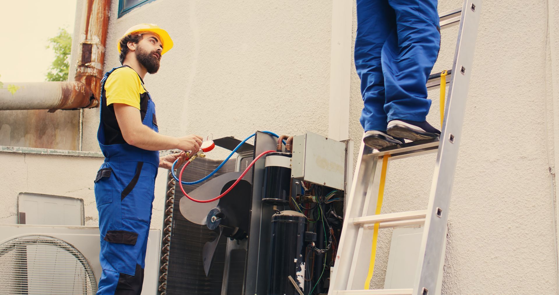 Two men are standing on a ladder working on a machine.