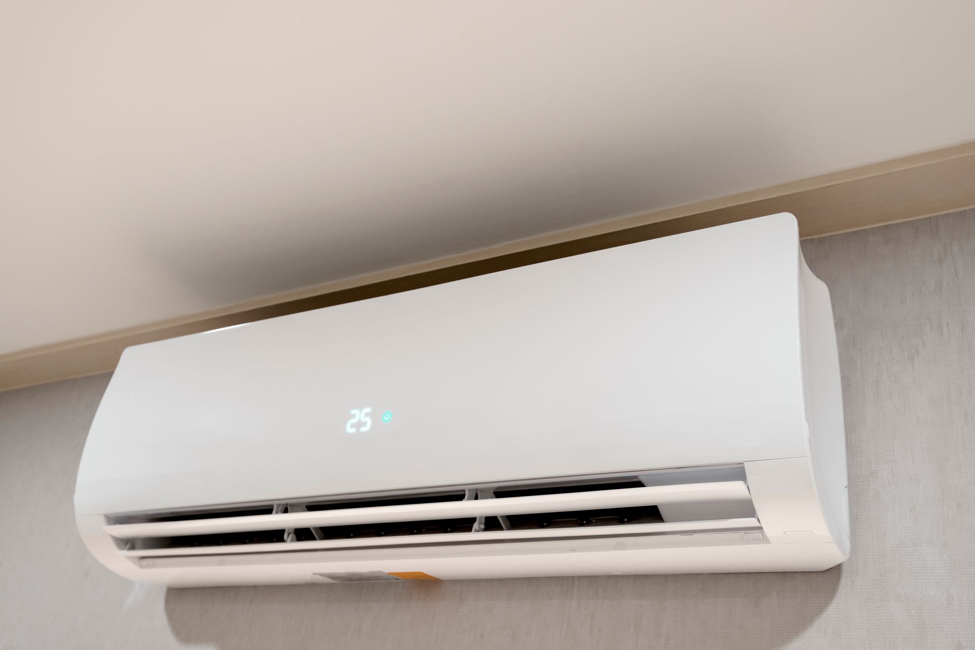 A white air conditioner is hanging on a wall and the temperature is 25 degrees