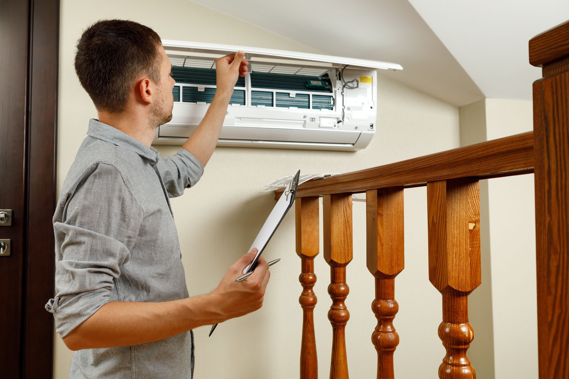 A man is looking at an air conditioner while holding a clipboard.