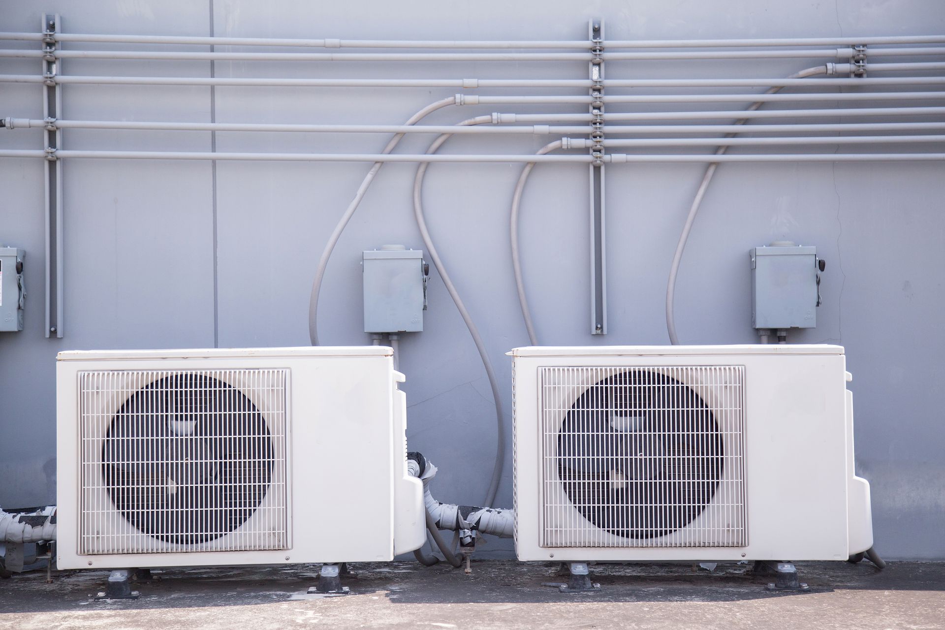 Two air conditioners are sitting next to each other on the side of a building.