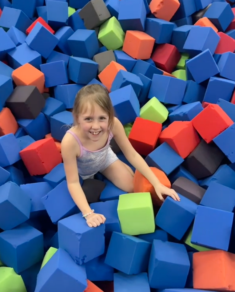 A little girl is sitting in a pile of foam cubes