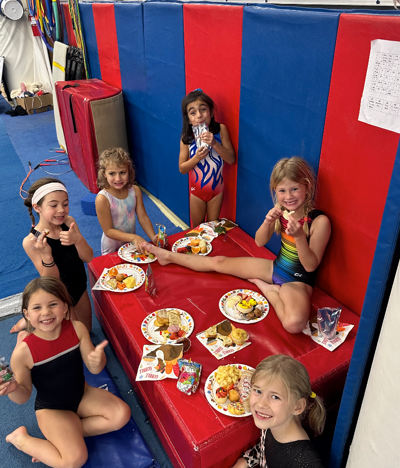 A group of young girls are sitting around a table with plates of food.