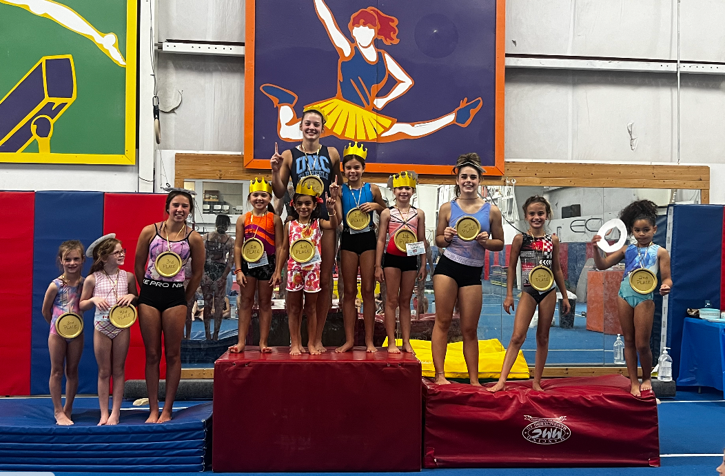 A group of young girls are standing on a podium in a gym holding medals.