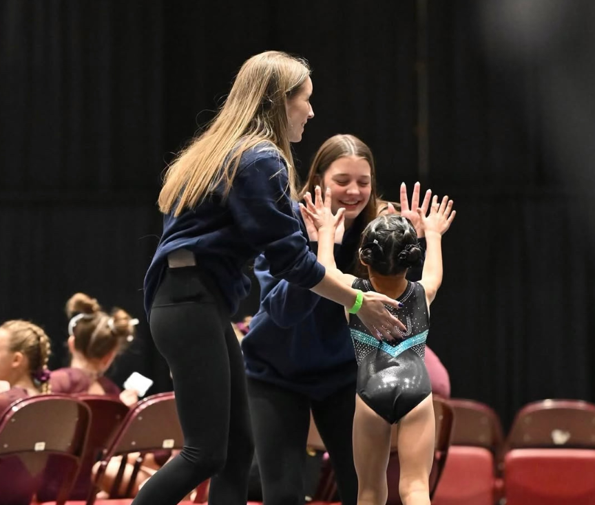 Two women are standing next to a little girl in a leotard.