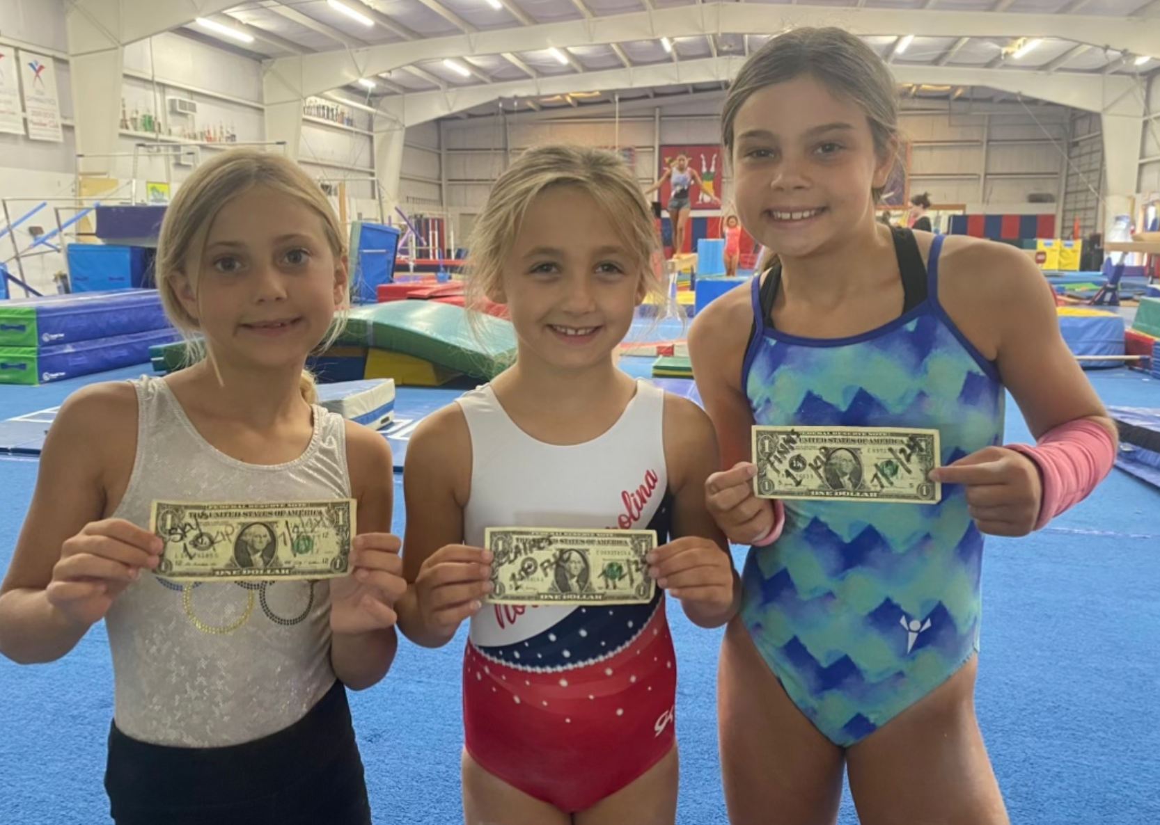 Three young girls are holding up dollar bills in a gym