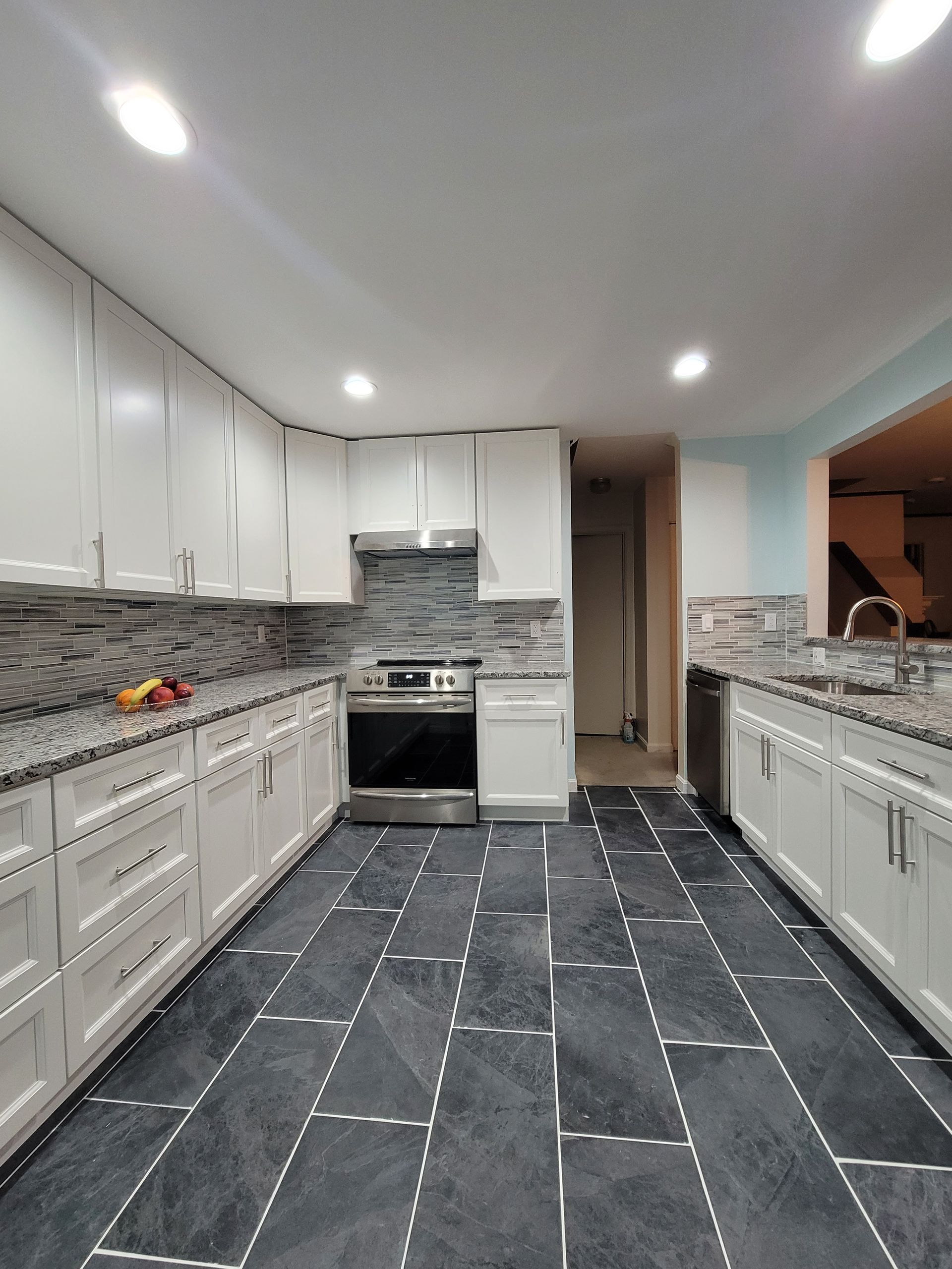Elegant white kitchen with large island, stainless steel appliances, and dark wood floors.