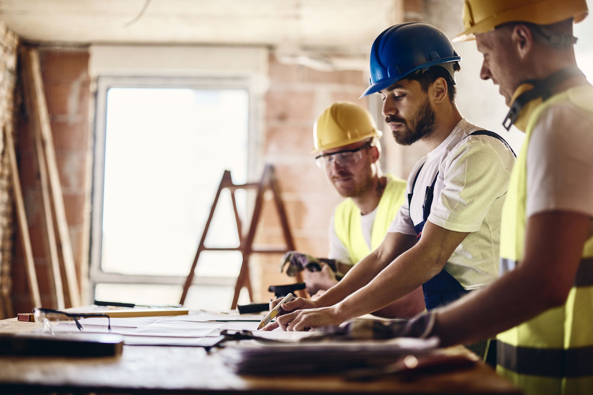 Construction workers in hard hats reviewing blueprints on a table at a job site.