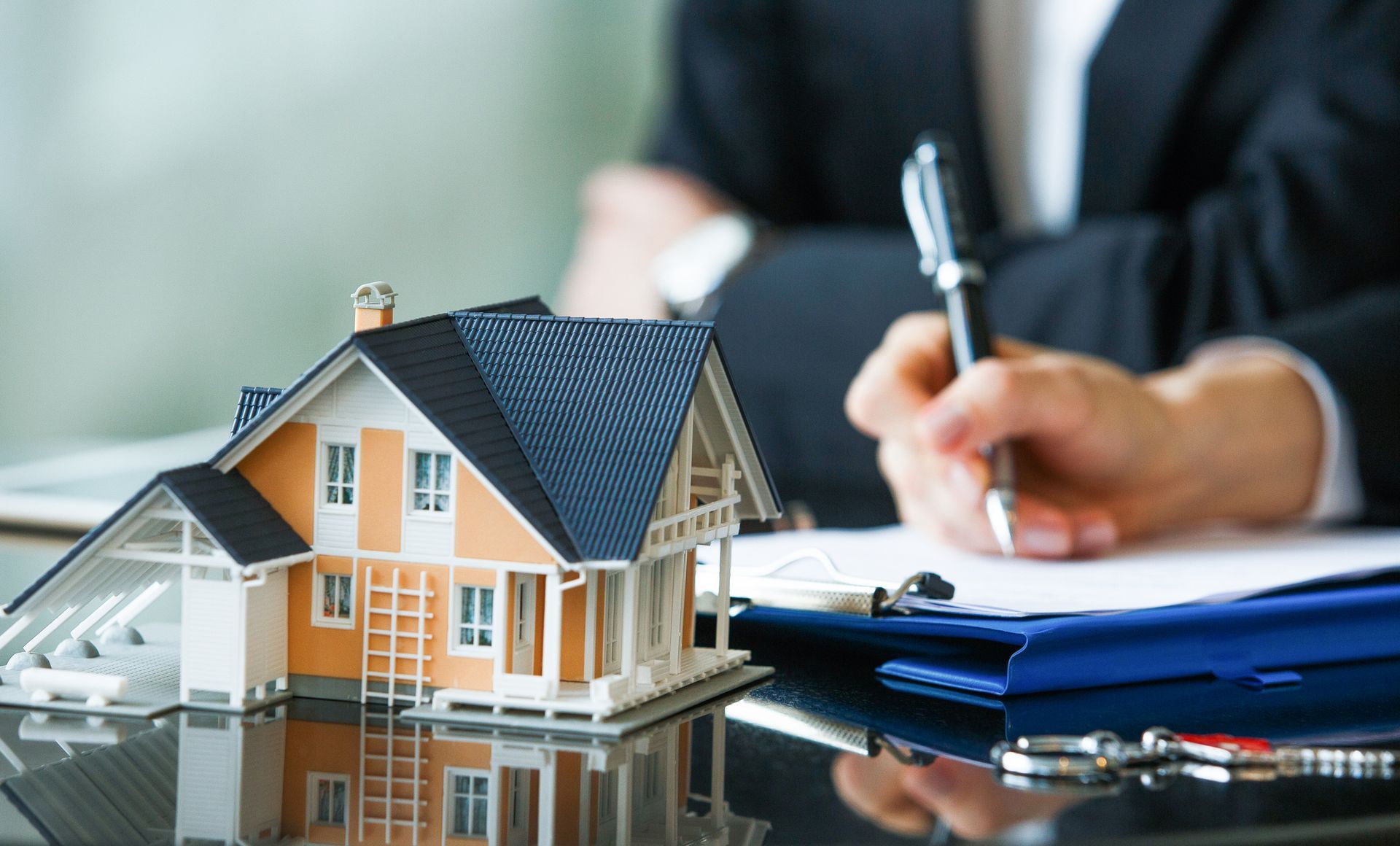 A small model house next to a person signing documents.