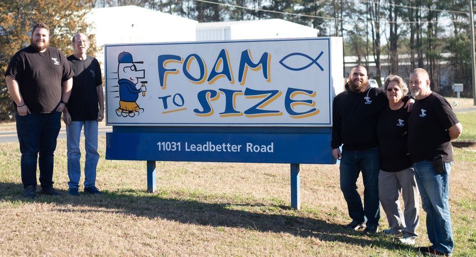 A group of men standing in front of a sign that says foam to size
