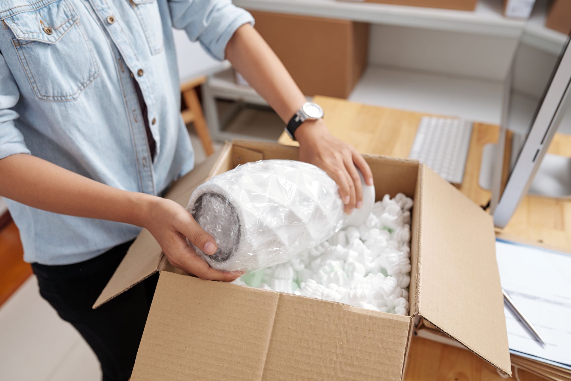 A woman is putting a vase in a cardboard box.