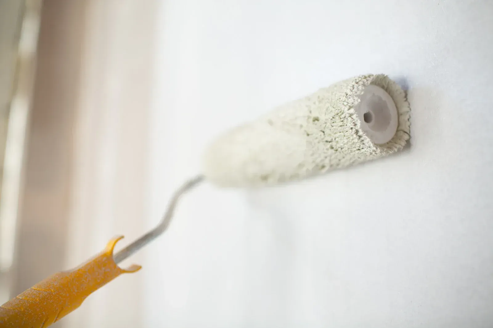 A paint roller is being used to paint a white wall.