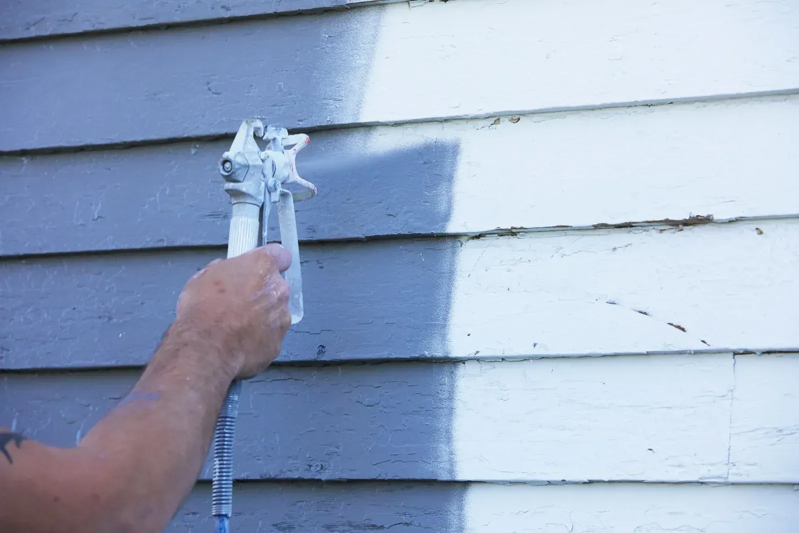 A person is spraying paint on the side of a house.