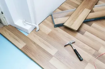 A hammer is laying on a wooden floor next to a door.