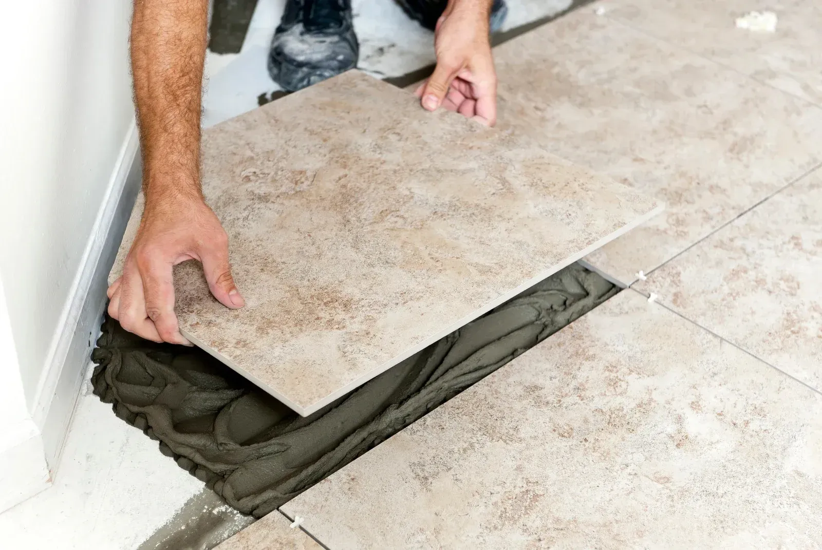 A man is laying a tile on a floor.