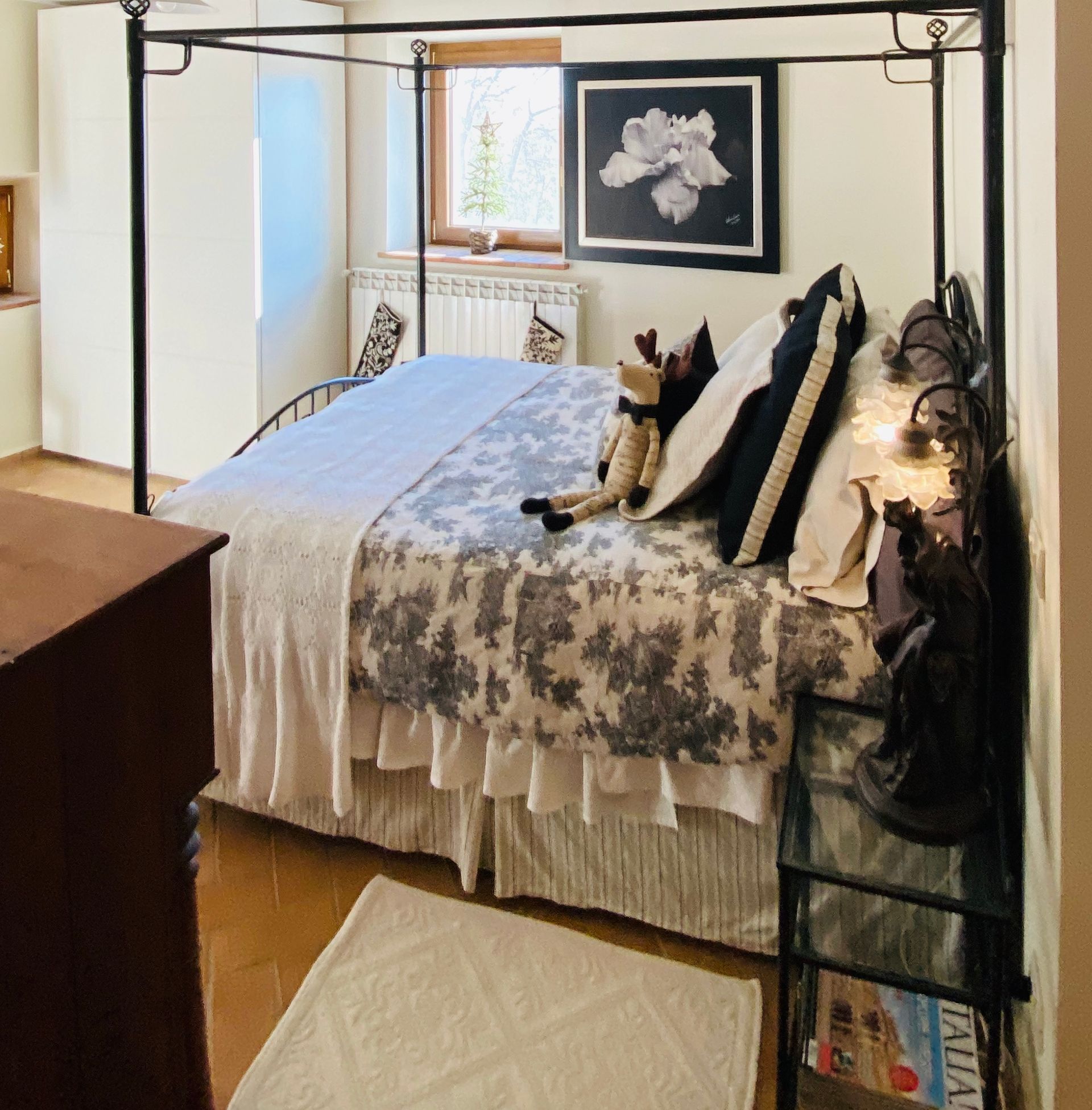 A bedroom with a black metal four-poster bed, floral bedding, a white rug, and a framed black-and-white flower print.